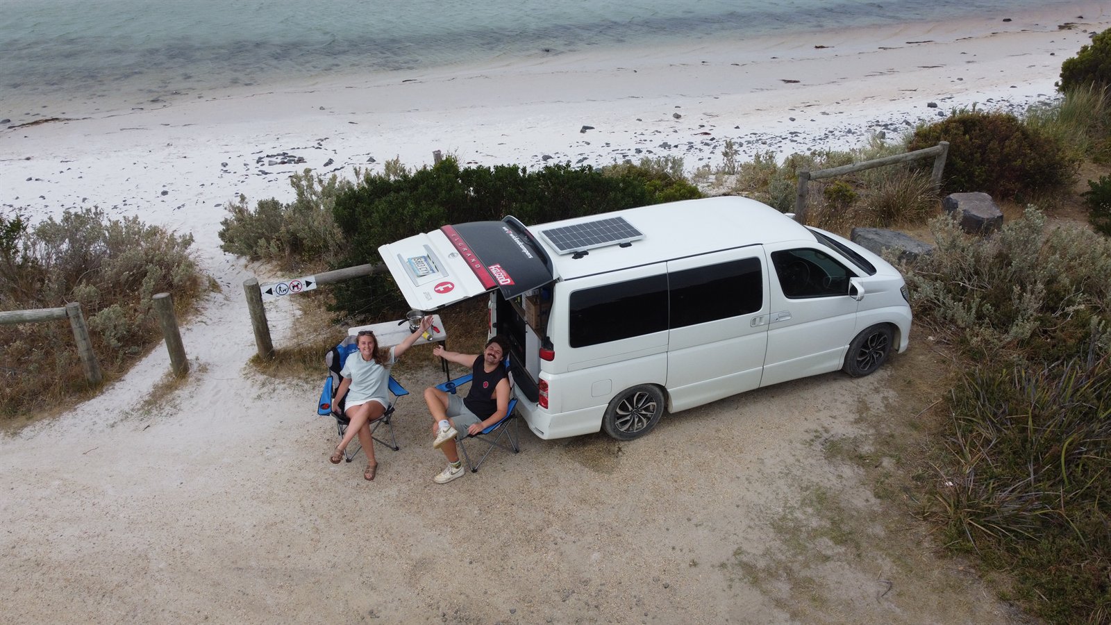 Two travellers relaxing beside a Wicked campervan near Ansons Bay